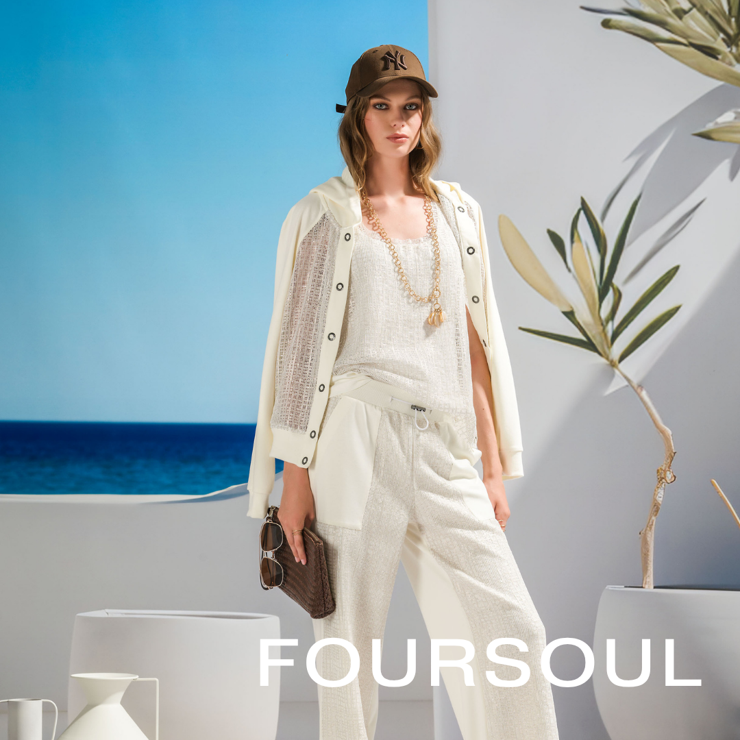 Fashion model in summer outfit with a brown cap, white cardigan, and cream-colored pants, holding sunglasses, standing in front of a beach scene background with a potted plant, promoting FOURSUL.