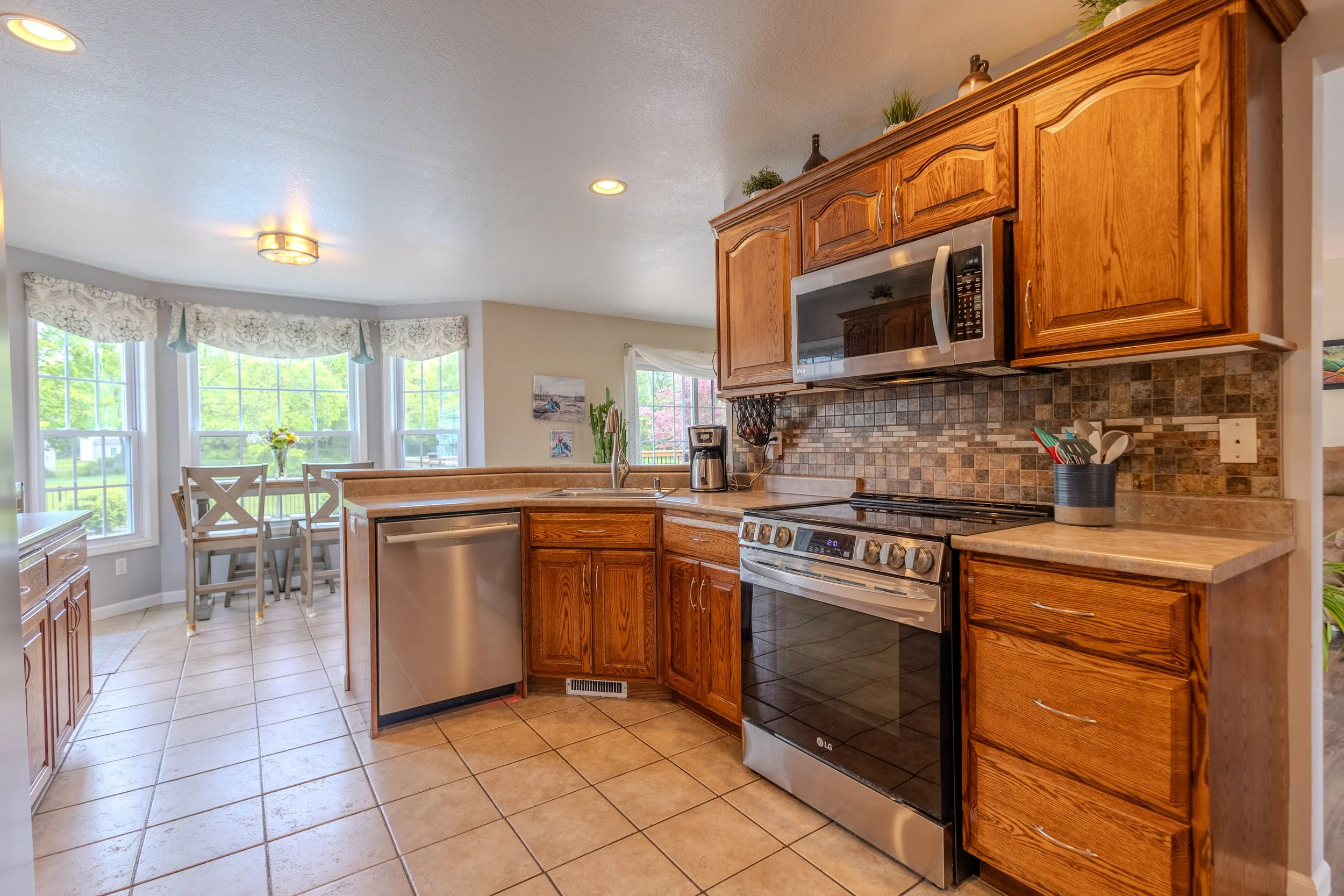 Kitchen with wooden cabinets, stainless steel appliances, tile flooring, and a dining area with large windows.