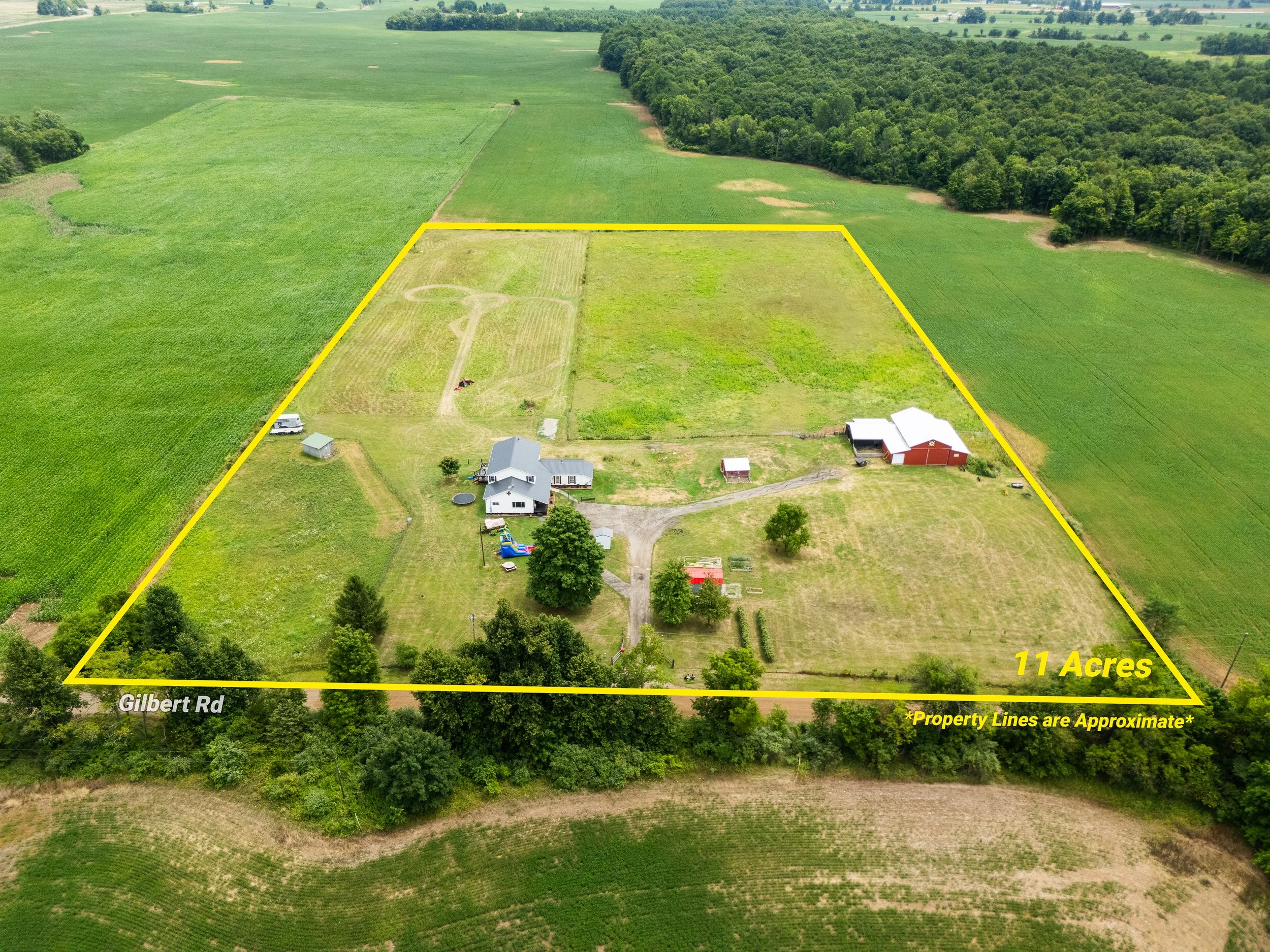 Aerial view of farmland with property boundary outlined in yellow, indicating 11 acres of land with houses, barns, and pastures, along Gilbert Road.