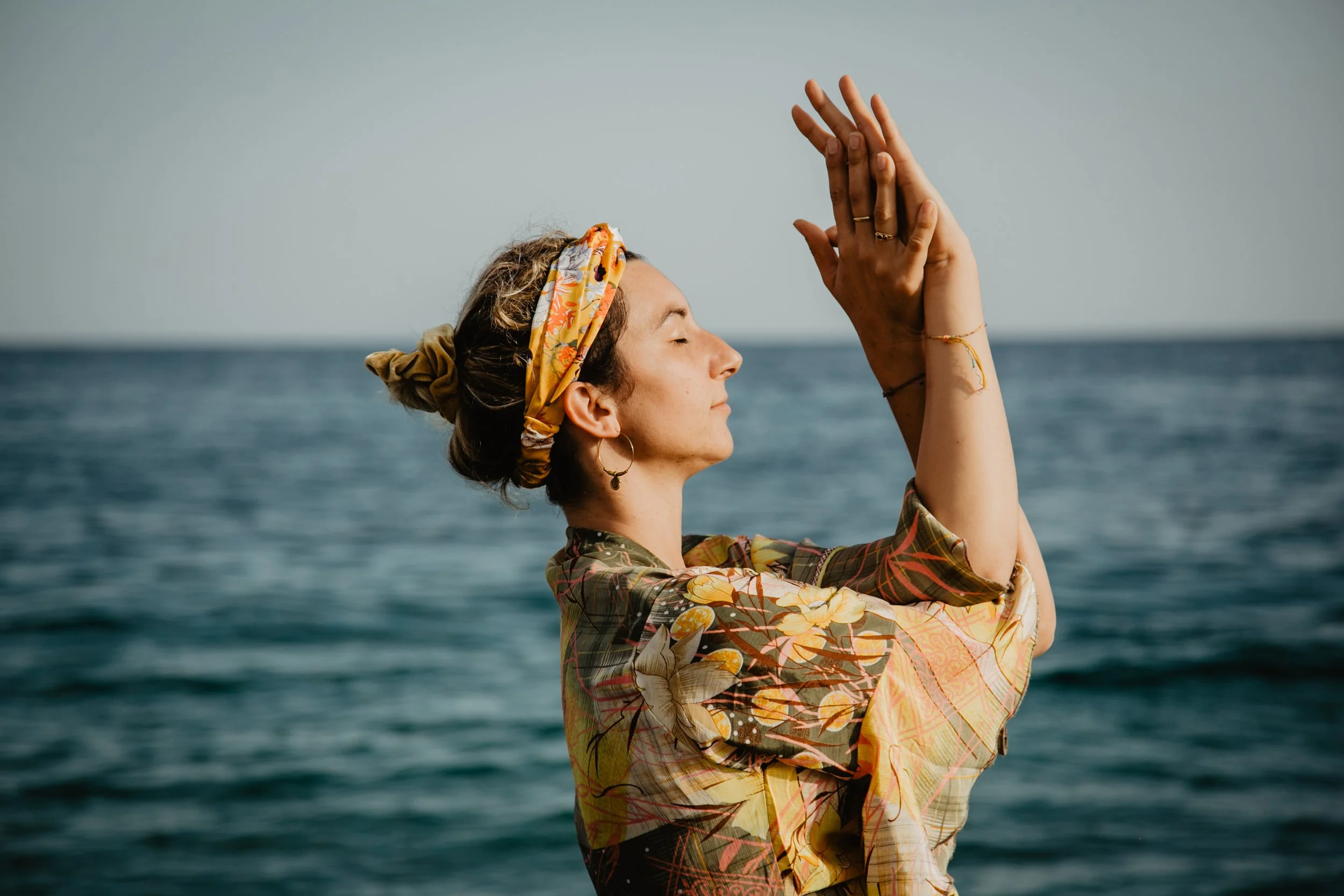 Una donna che fa yoga davanti al mare con le mani unite in posizione di preghiera.