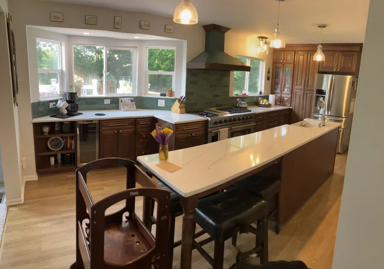 A newly remodeled kitchen in Cincinnati featuring quartz countertops, a large island with pendant lighting, and sleek cabinetry. A designer and homeowner review plans together, highlighting collaboration and attention to detail.