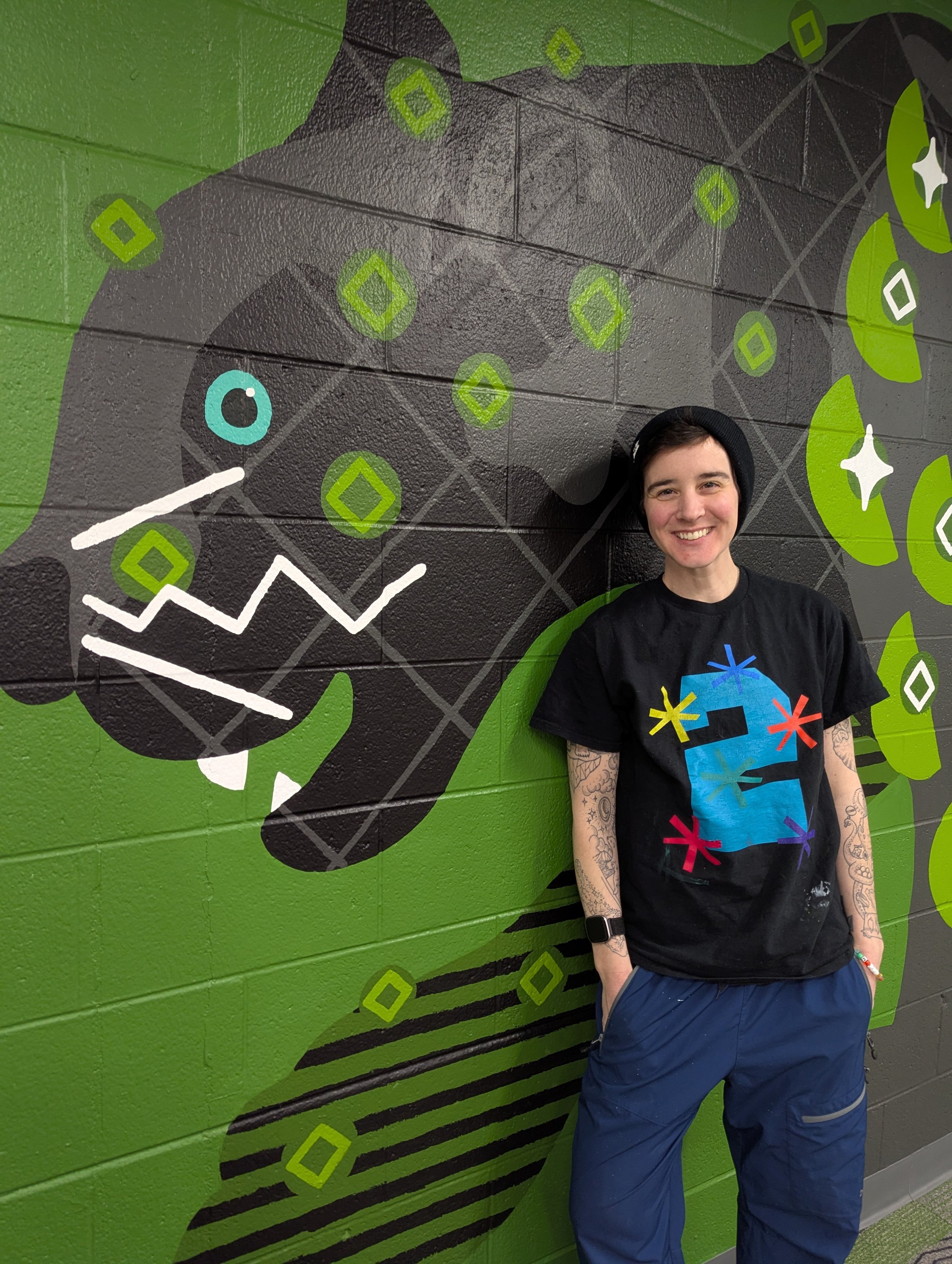 Artist Hannah Tews standing in front of a cropped section near the black panther’s head on the elementary school animal mural.