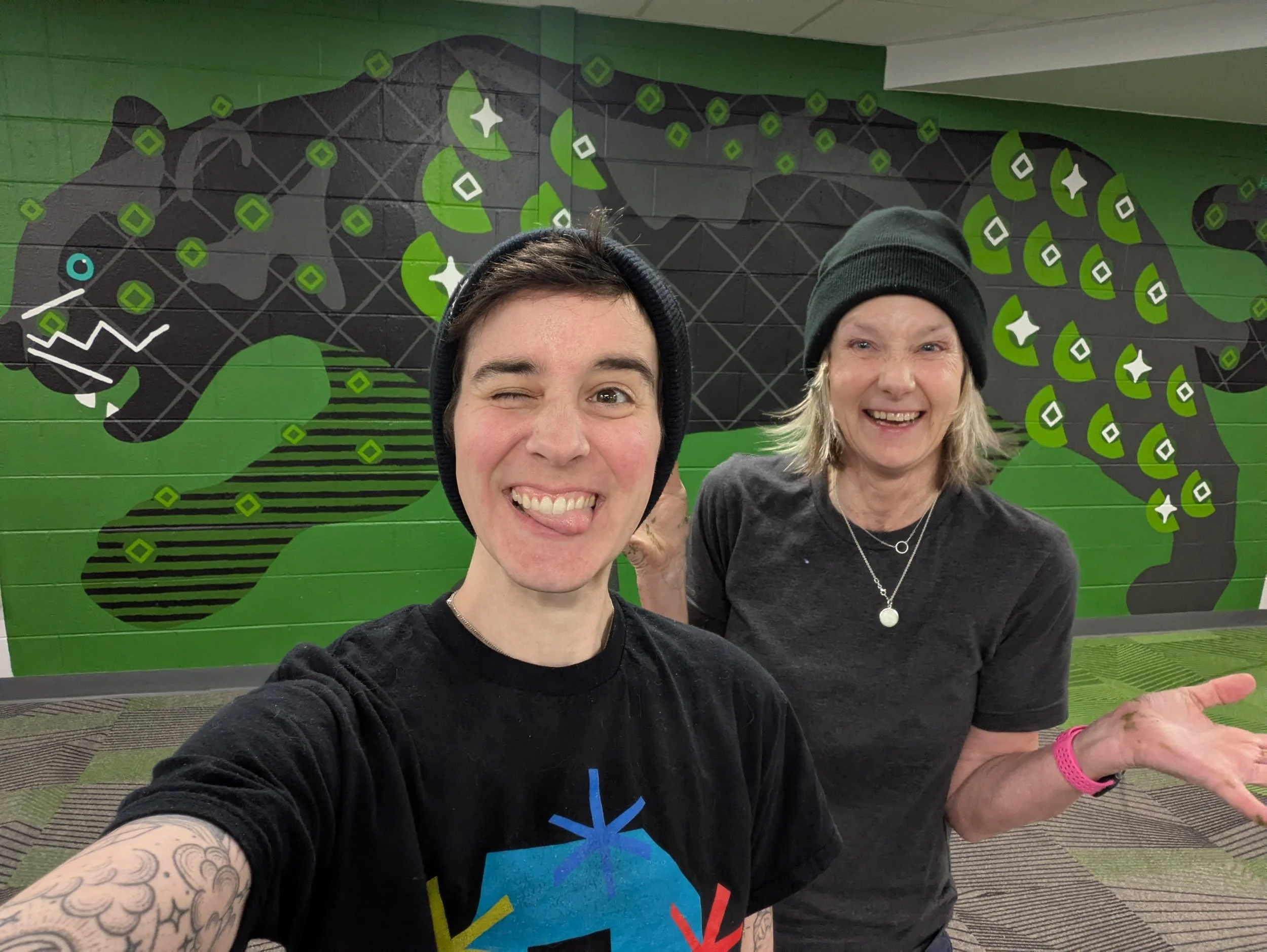 Artist Hannah Tews and second painter standing in front of completed black panther elementary school mural full wall.
