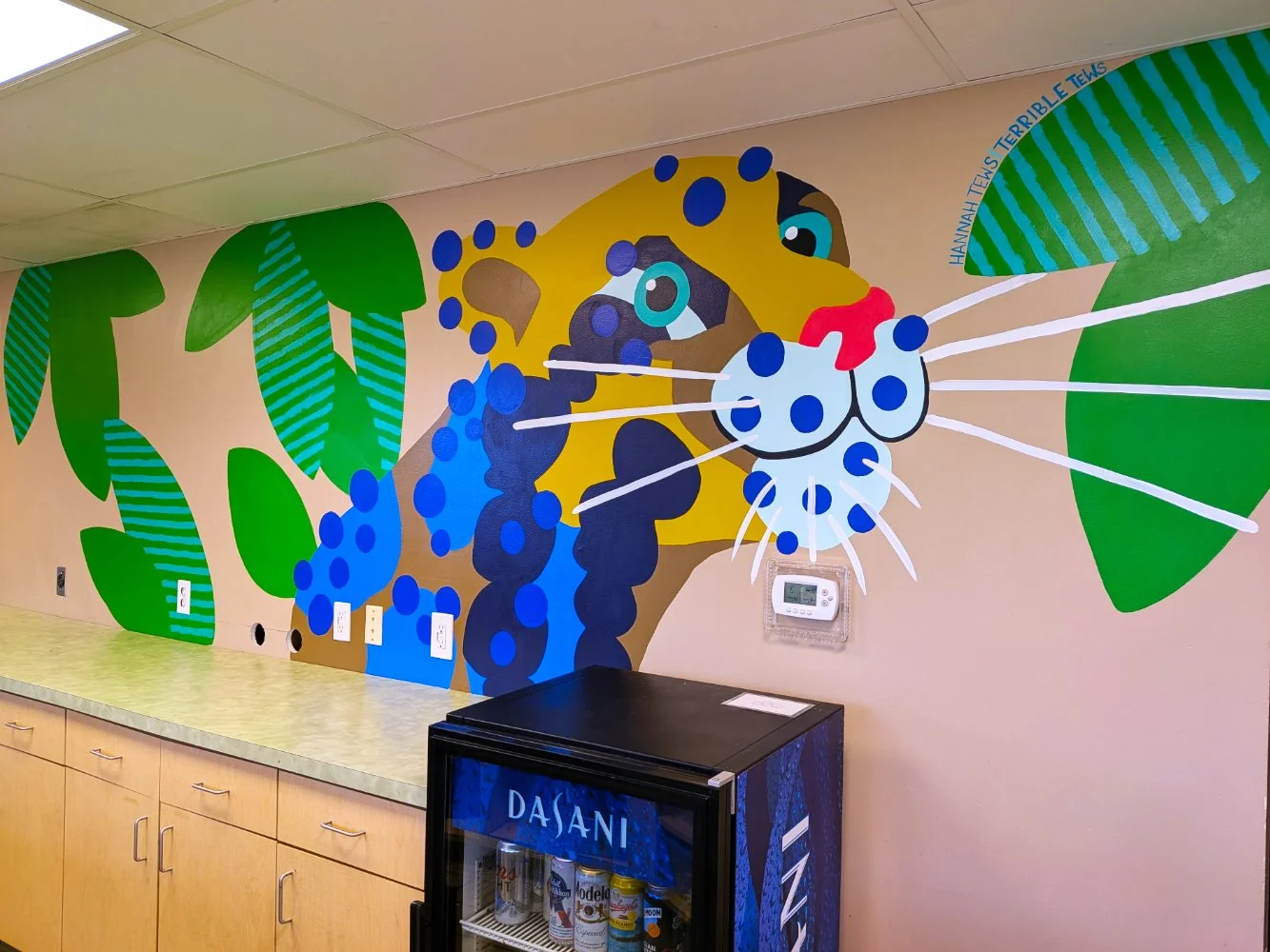 Clouded Leopard mural in the Jungle Grill Building at the Racine Zoo, showing a colorful jungle cat face and leaves with dots and stripes above a restaurant counter.