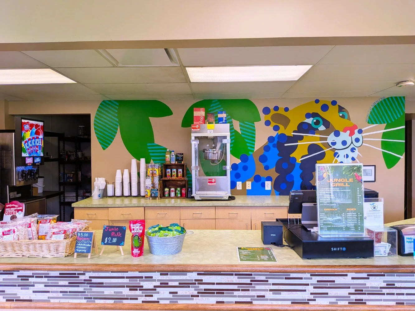 Clouded Leopard mural in the Jungle Grill Building at the Racine Zoo, showing a colorful jungle cat face and leaves with dots and stripes above a busy restaurant counter.