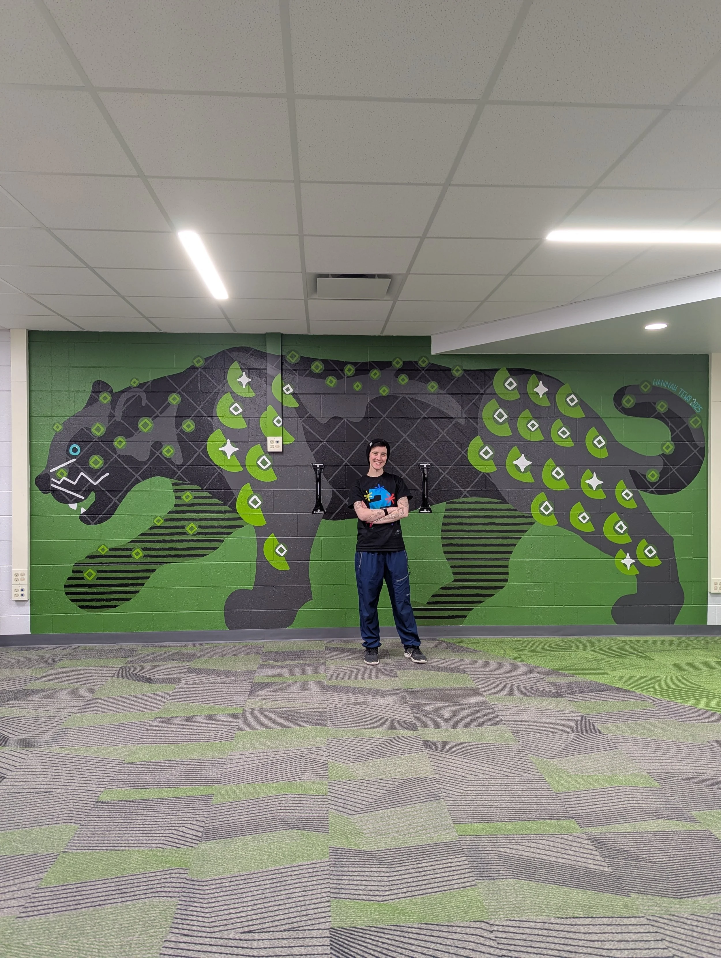 Full wall shot of artist Hannah Tews standing in front of the complete black panther animal mural.