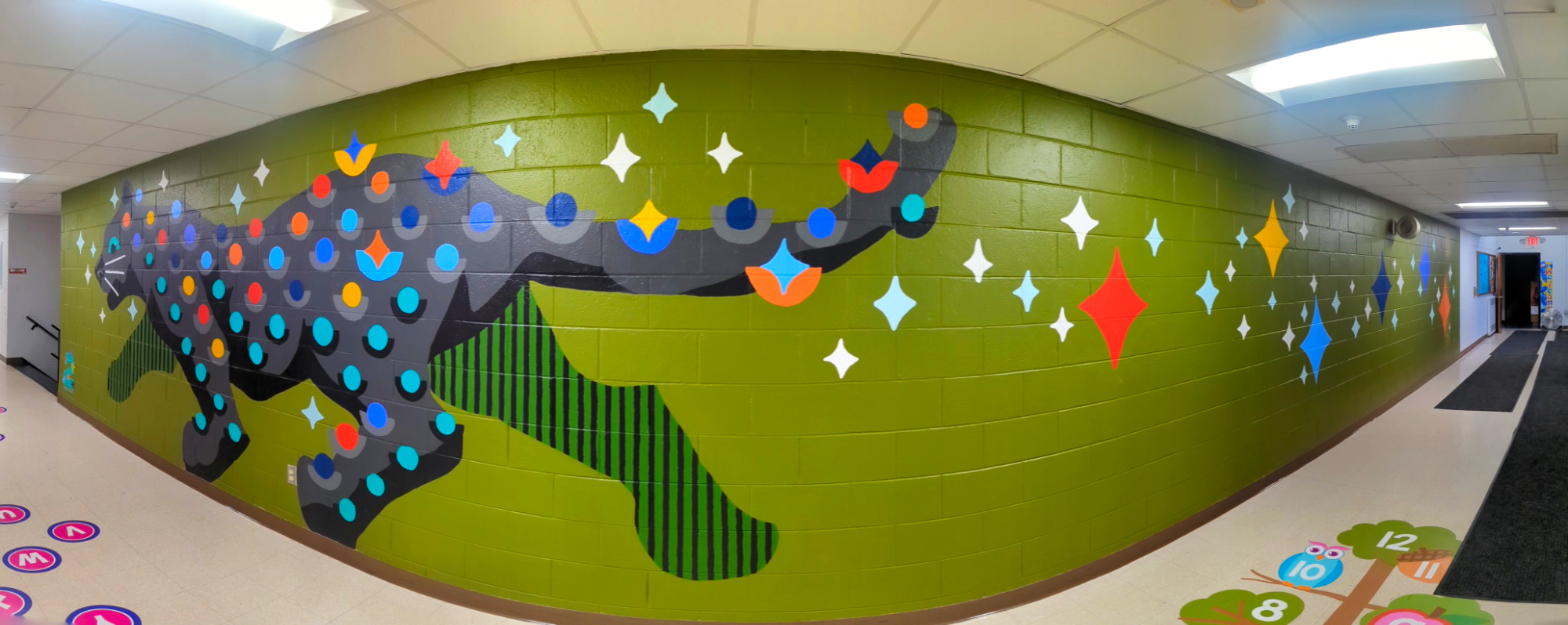 Panoramic image of Bright Star Panther mural in an elementary school hallway, showing a black panther with colorful star and dot patterns.