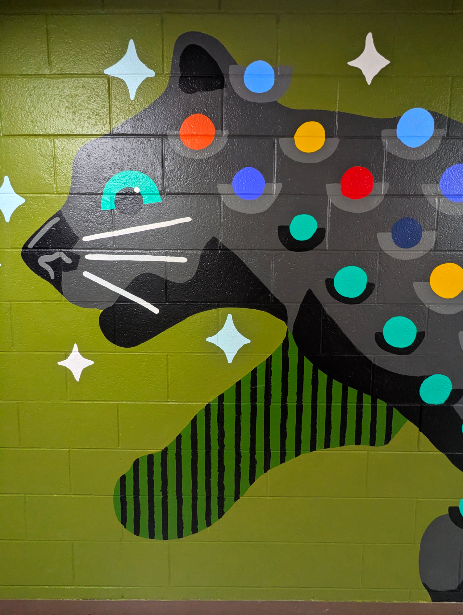 Bright Star Panther mural in an elementary school hallway, showing a black panther with colorful star and dot patterns cropped on face and front leg.
