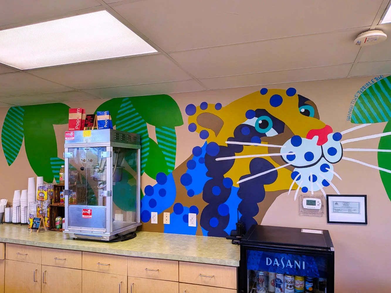 Clouded Leopard mural in the Jungle Grill Building at the Racine Zoo, showing a colorful jungle cat face and leaves with dots and stripes above a restaurant counter.