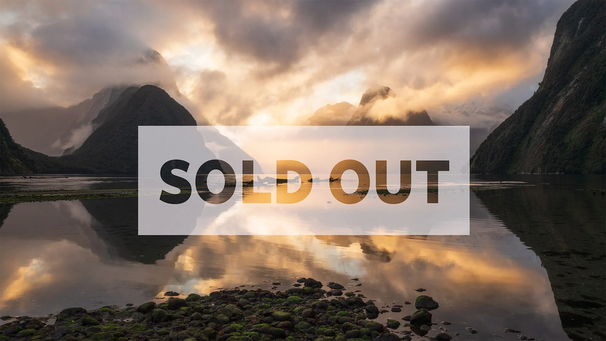 A scenic landscape of mountains surrounding a calm body of water reflecting the sky and mountains, with the moon visible among clouds at sunset or sunrise. The word SOLDOUT is overlaid in large, semi-transparent text.