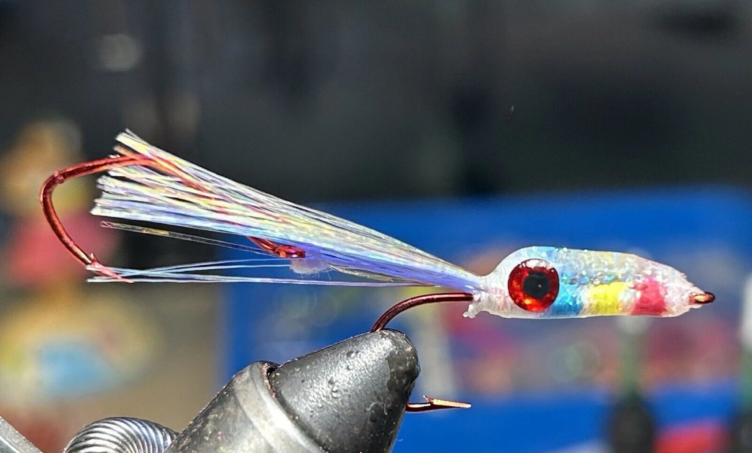 Close-up of a colorful fishing lure with wings, held by a person's hand in a metallic glove.