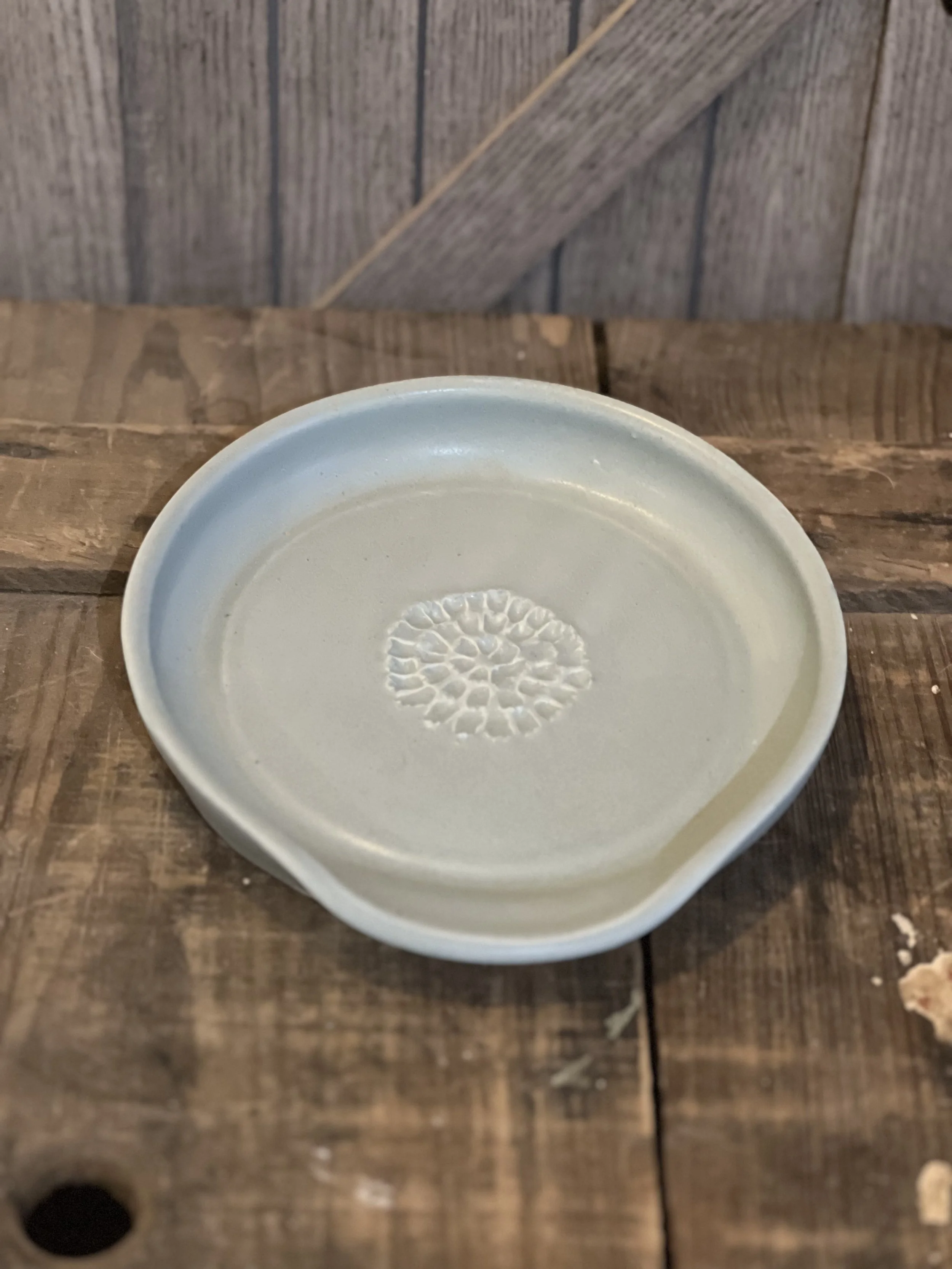 A small, round ceramic dish with a textured circular pattern in the center, placed on a rustic wooden surface.