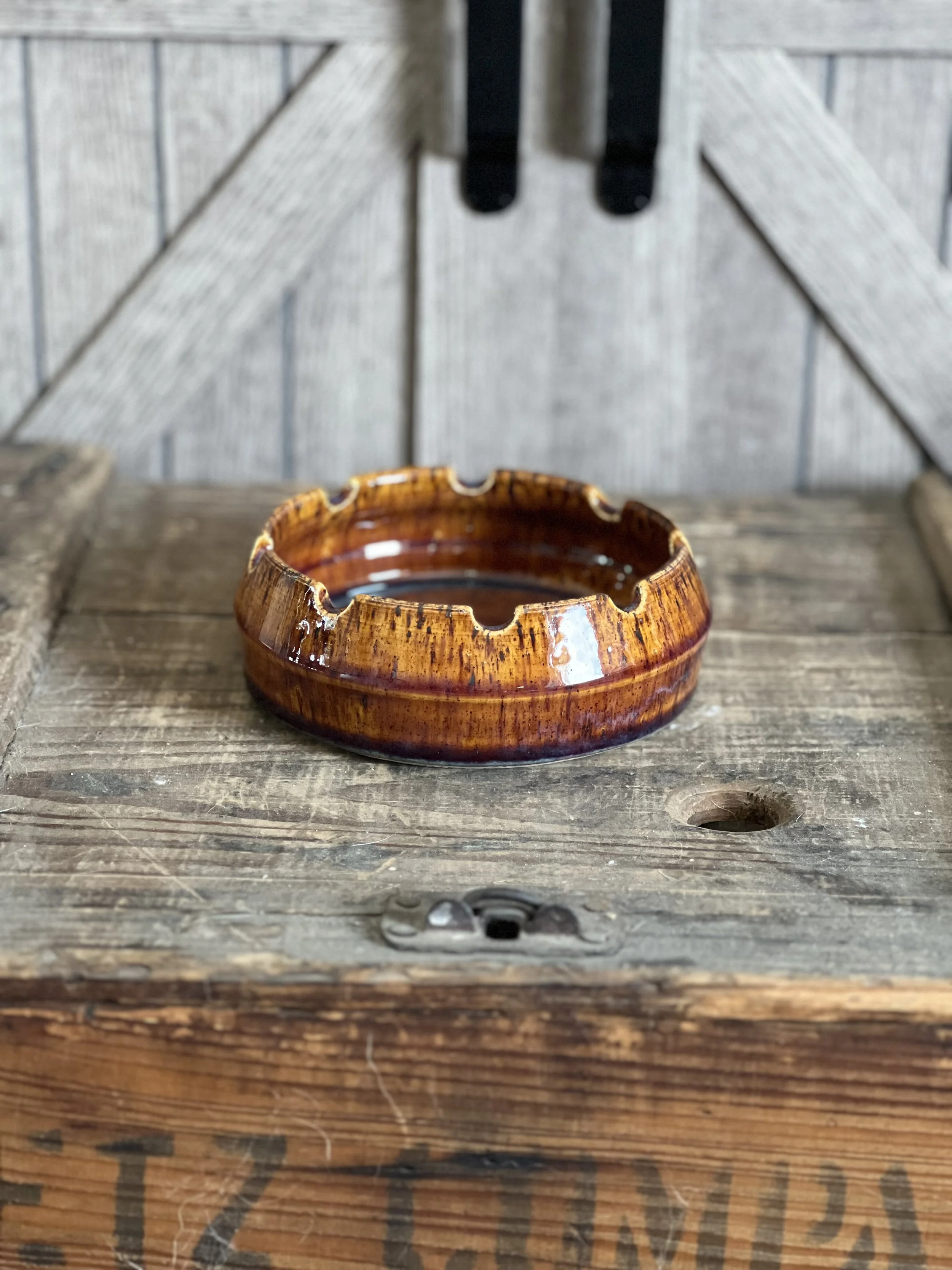 A brown ceramic ashtray on a weathered wooden surface with a rustic background.