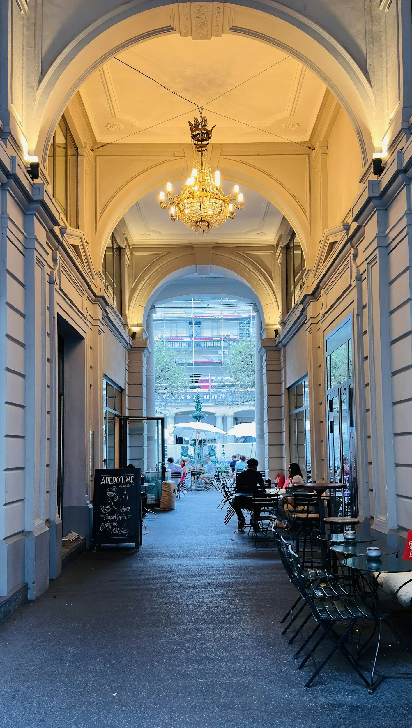 Inside view of a cafe or restaurant with ornate archways, a chandelier, and outdoor seating area visible through the arches.