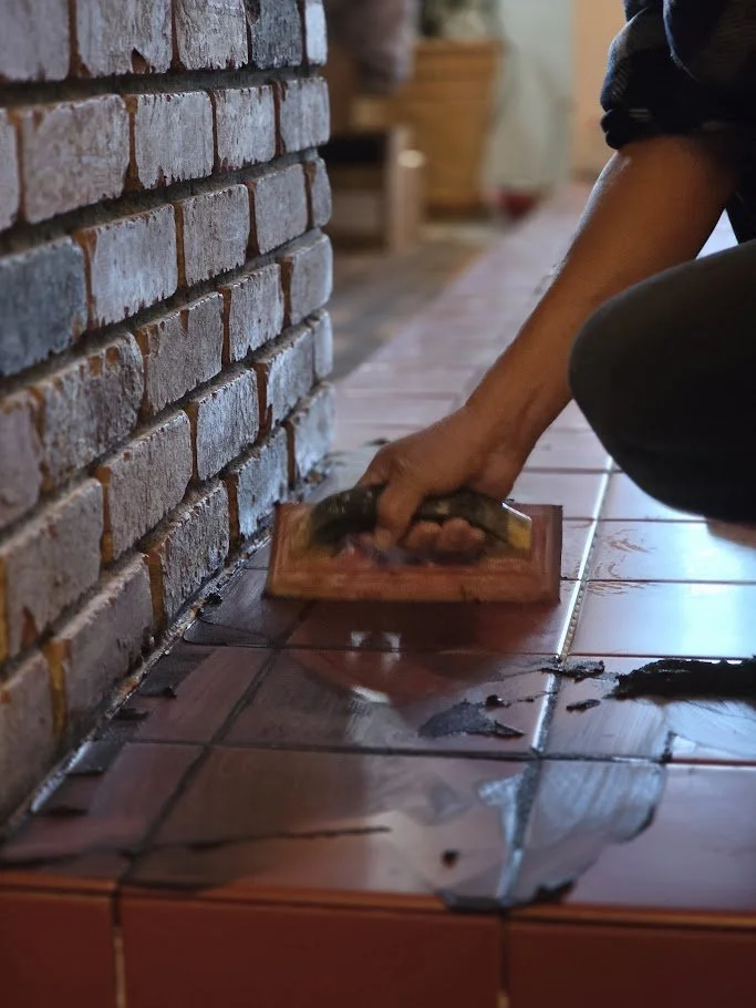 Black grout being installed between red floor tiles to create contrast and definition.