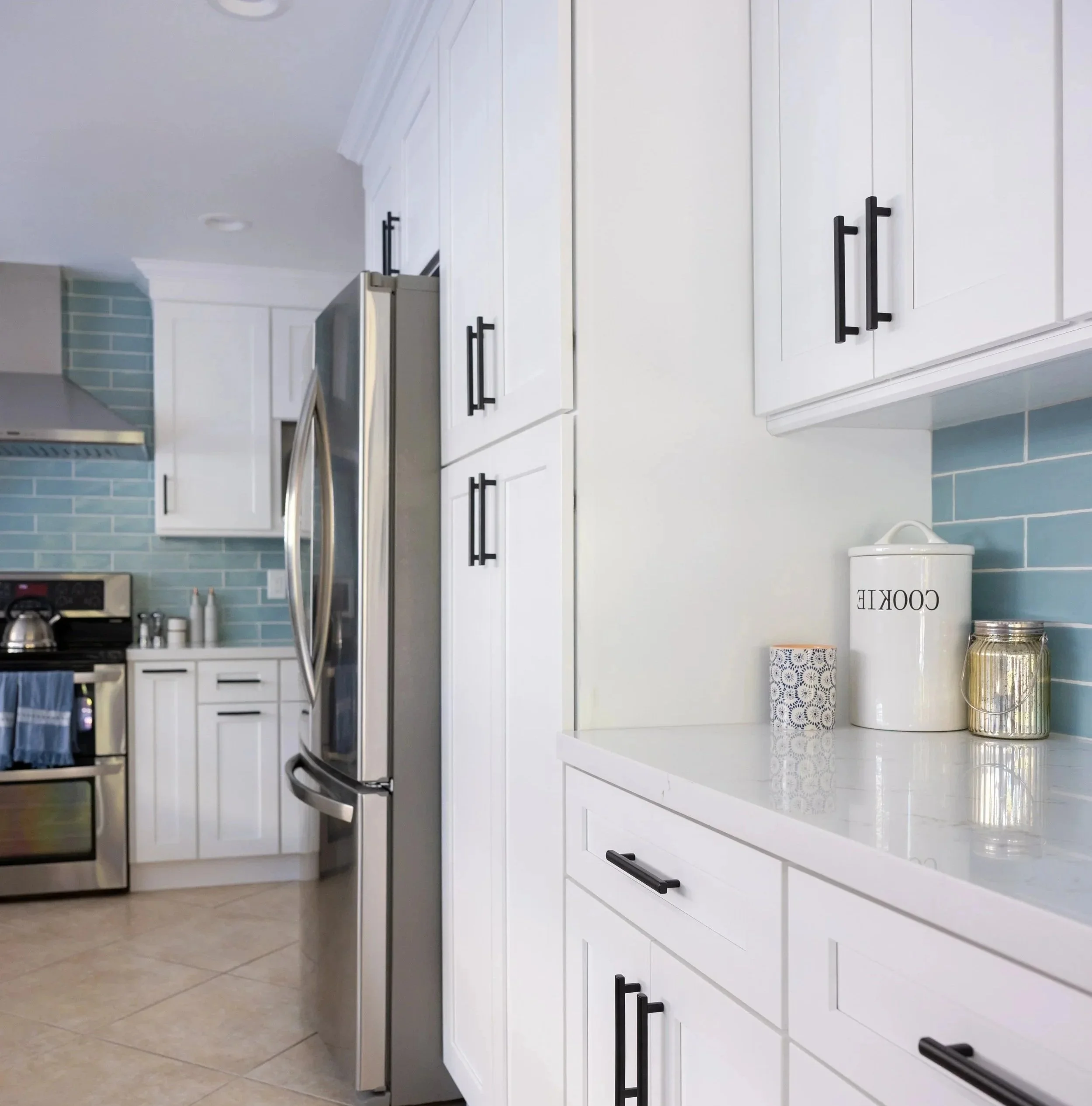 Clean, modern kitchen with white cabinets, black handles, stainless steel appliances, a light blue subway tile backsplash, and decorative jars on the counter. Contemporary kitchen remodel