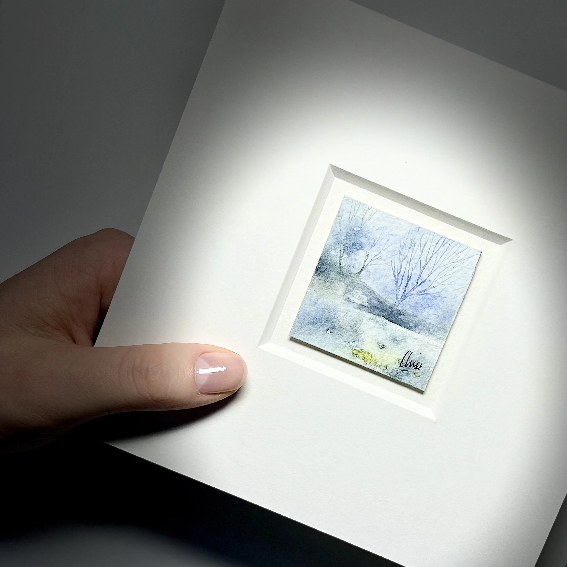Hand holding Lakeside watercolour painting, under spotlight