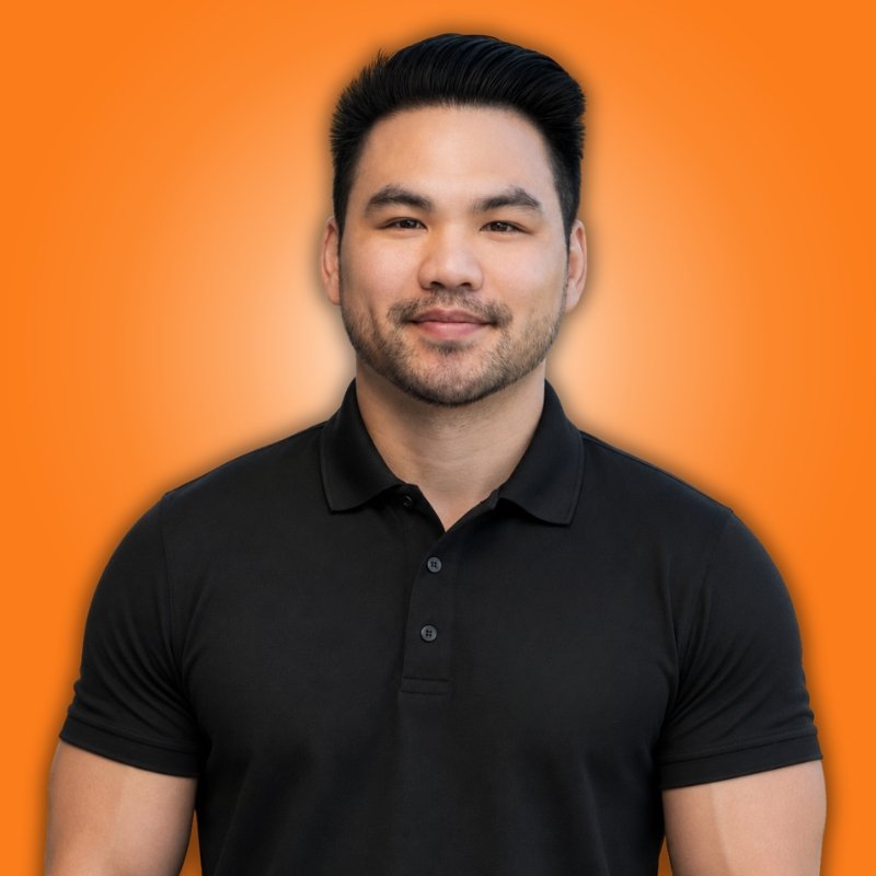 Man with crossed arms in black t-shirt, tattooed arm, wearing a smartwatch, white background with orange circular border.