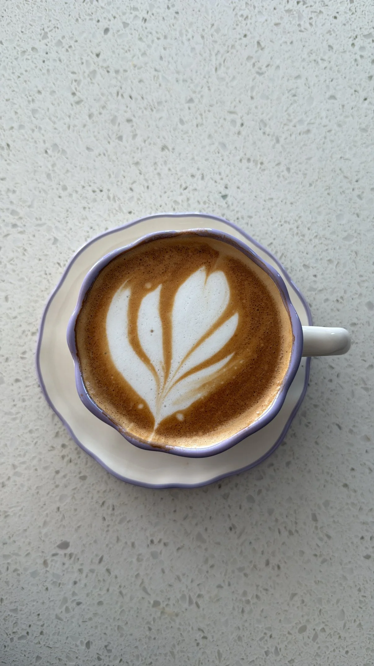 A cup of coffee with foam art in a purple and white cup on a white textured surface.