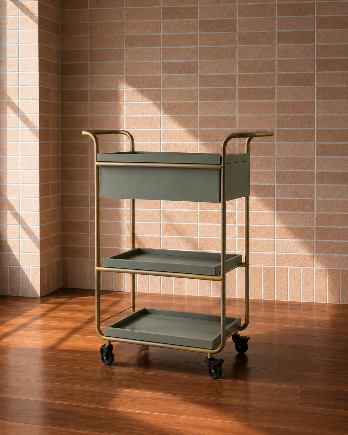 Empty metal and plastic utility cart with three trays on caster wheels, against a brick wall and hardwood floor.