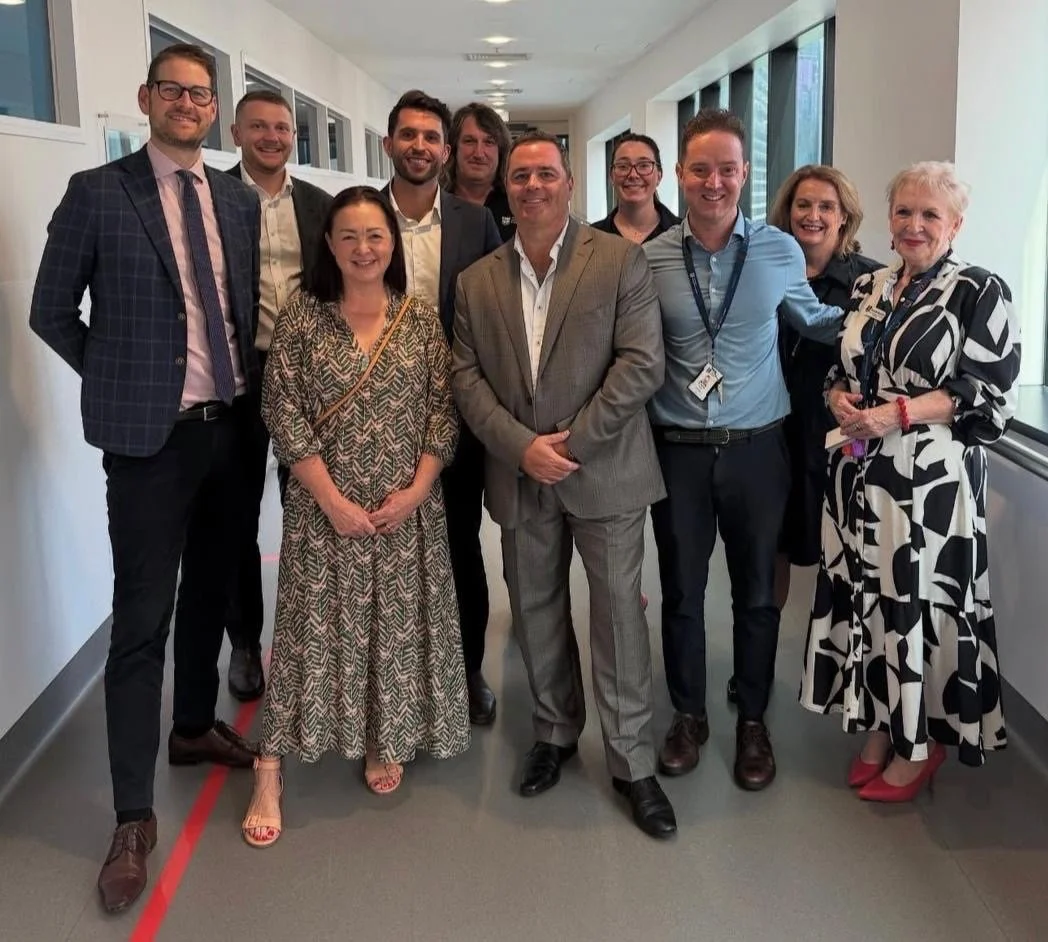 Group of ten professionally dressed people standing in a hallway, smiling at the camera.