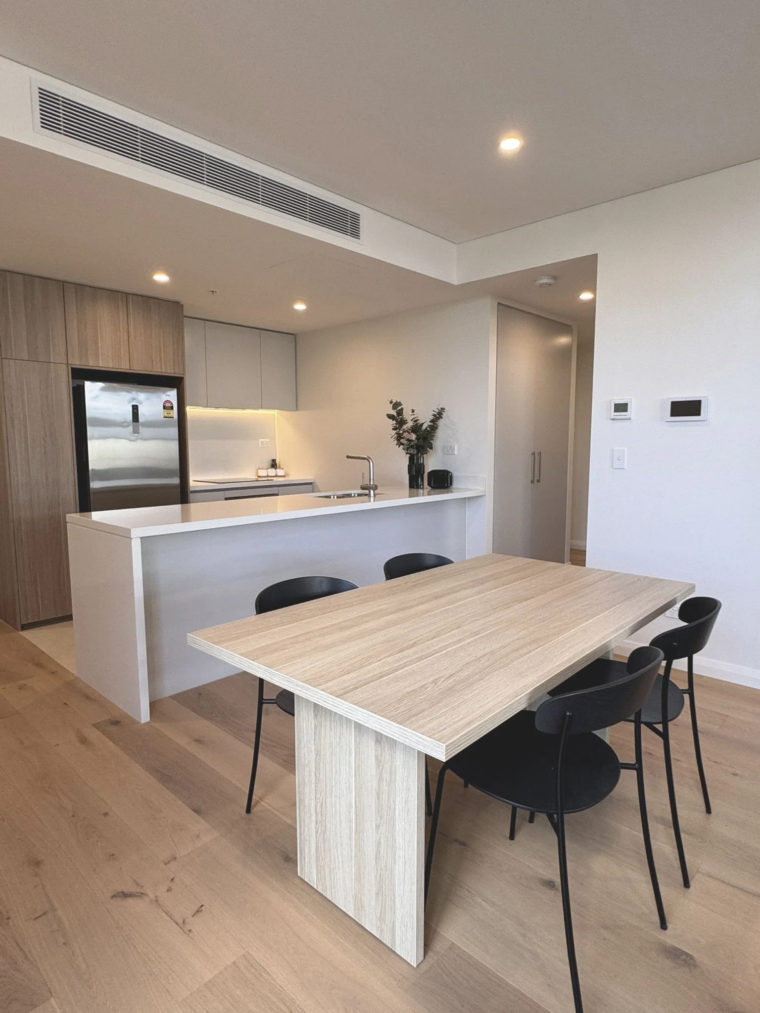 Modern open-concept kitchen and dining area with a wooden dining table and black chairs, white kitchen island, and minimalist decor.