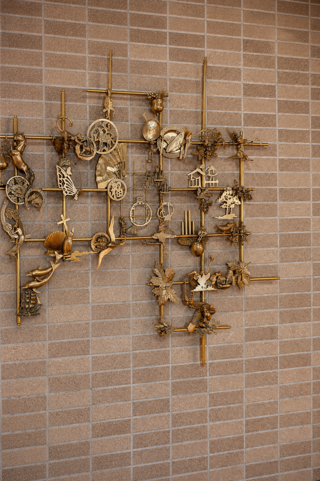 Decorative wall art gallery with gold-colored metal ornaments of various shapes and objects, mounted on a brick wall.