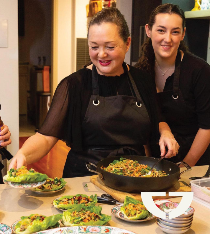 Two women preparing and serving salad bowls with leafy greens and vegetables in a kitchen.