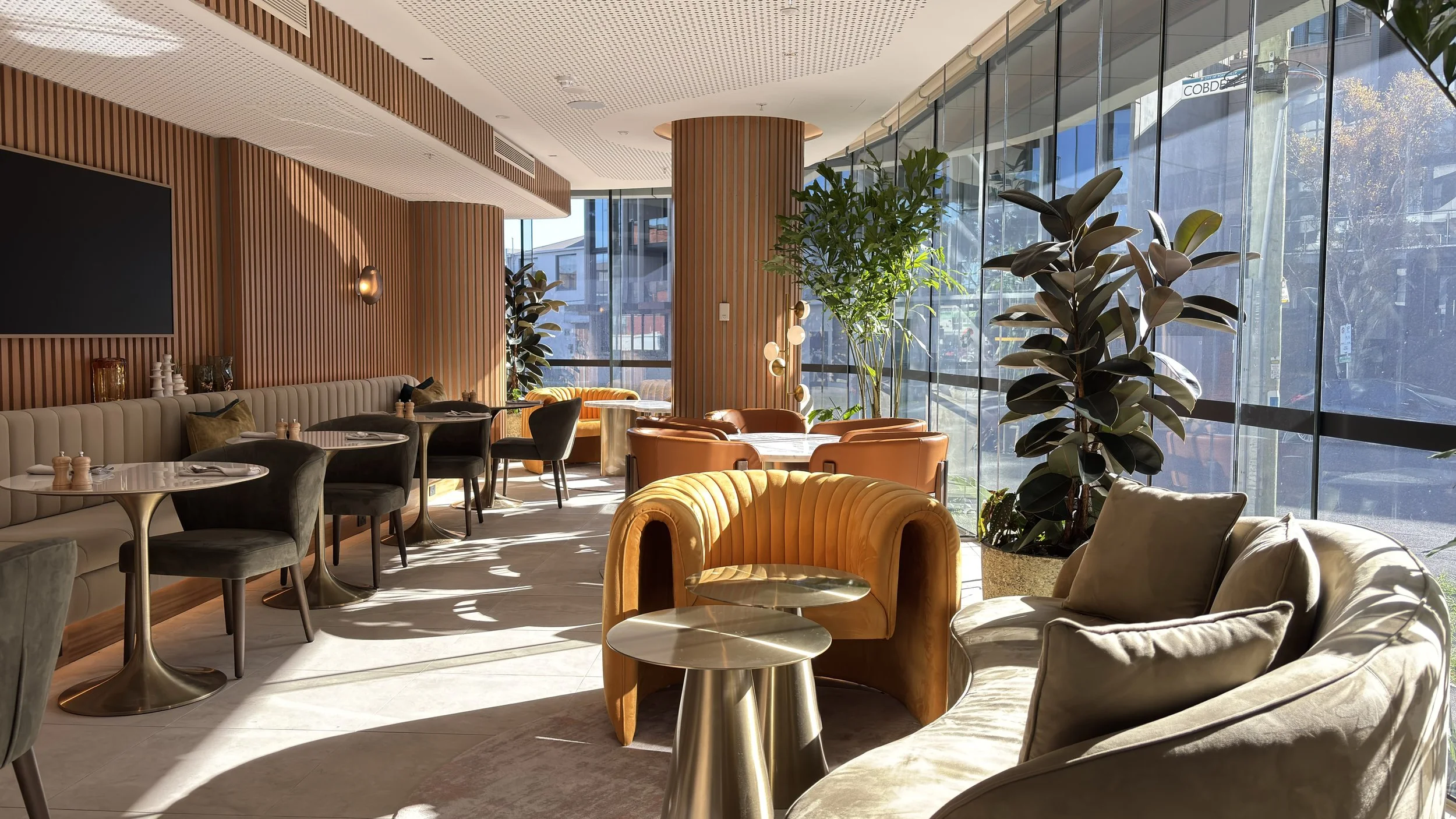 Modern indoor lounge area with large windows, green plants, and a variety of chairs and tables.
