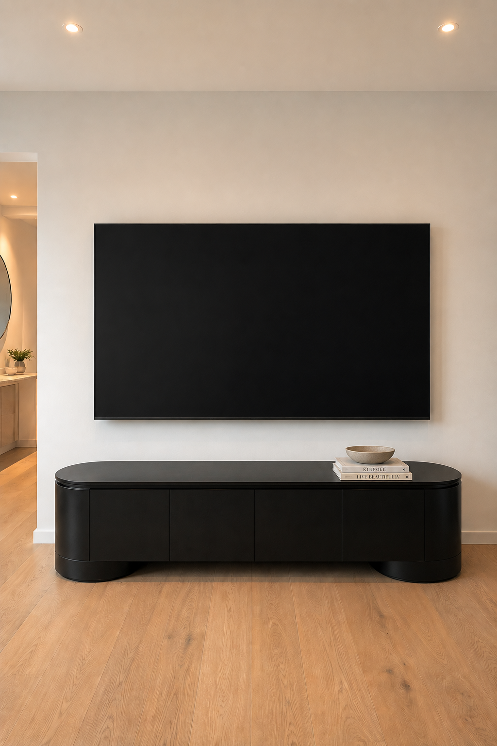 Living room with a large flat-screen TV mounted on a white wall, black modern console table below the TV, and a bowl with books on top.