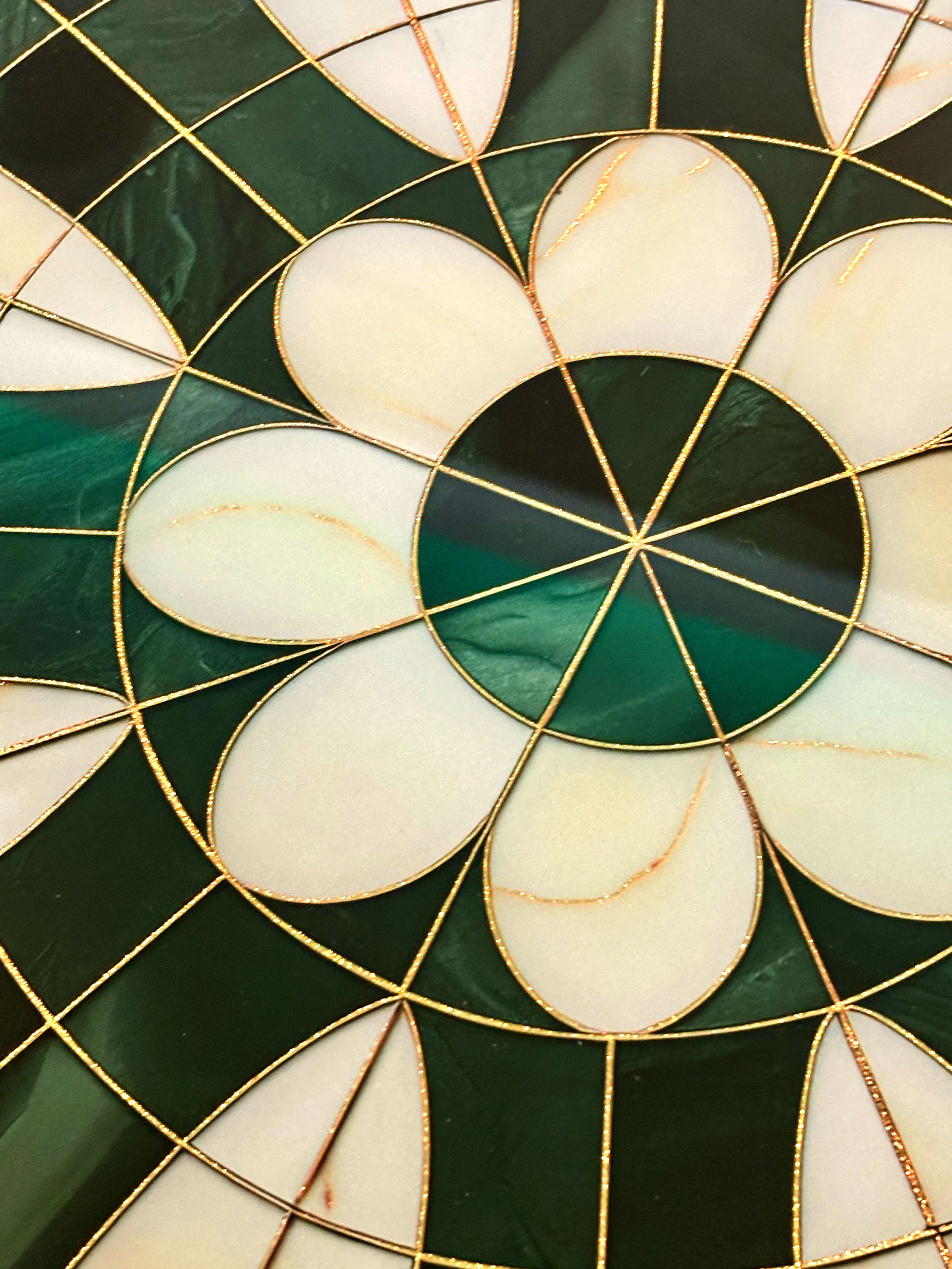 Close-up of stained glass artwork with green, white, and gold colors forming geometric patterns and floral shapes.