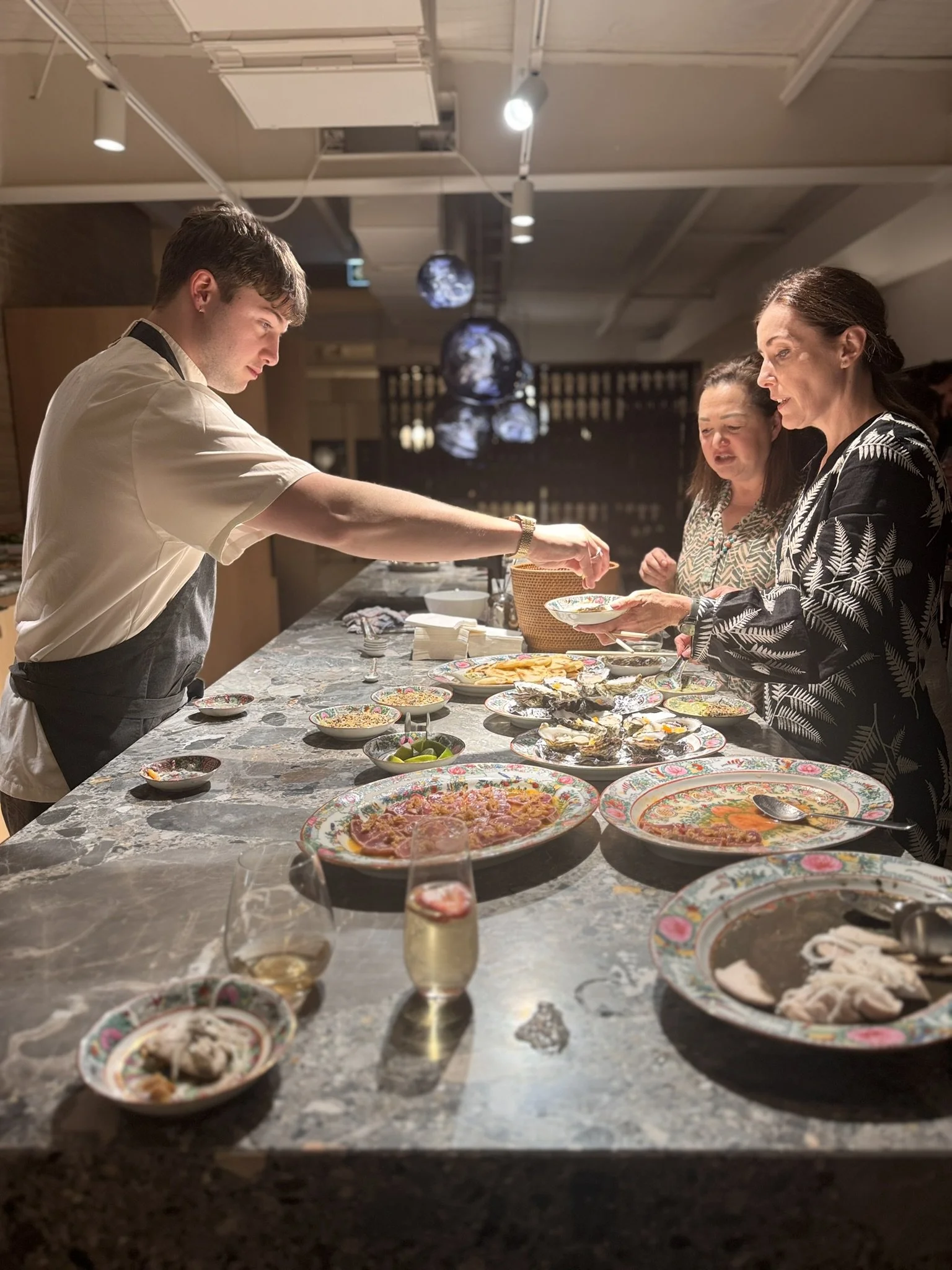 A group of people are serving themselves food from a buffet table filled with various dishes, including salads, seafood, and pizza, in a restaurant setting.