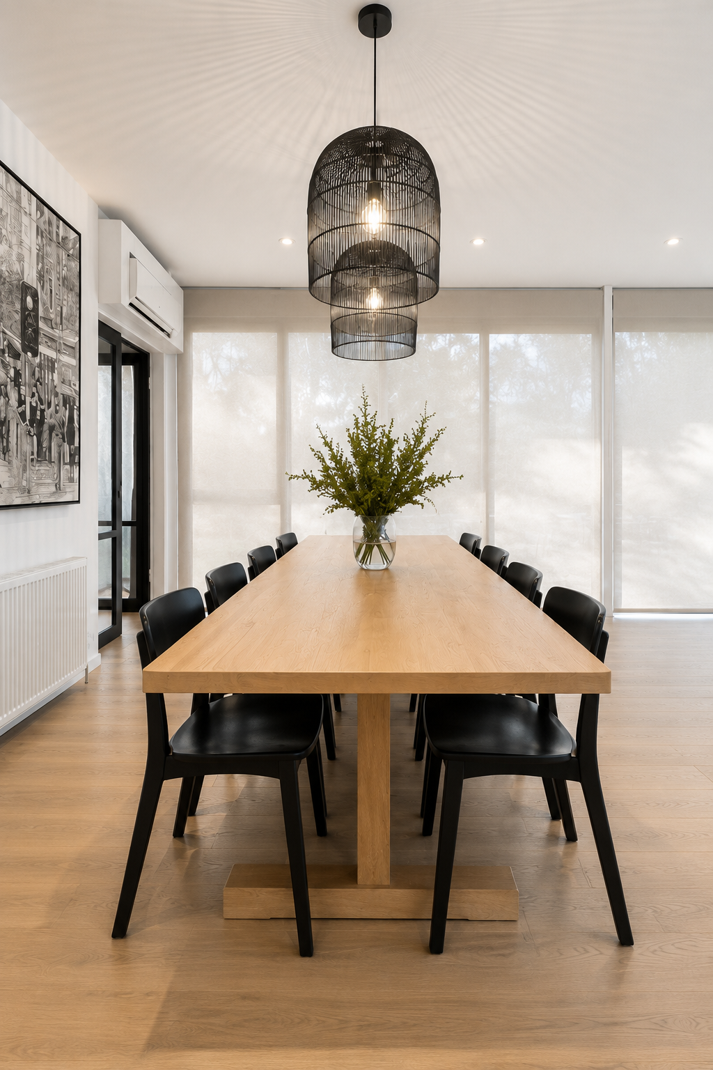Modern dining room with a wooden table, black chairs, a vase with green foliage, and a woven black pendant light.