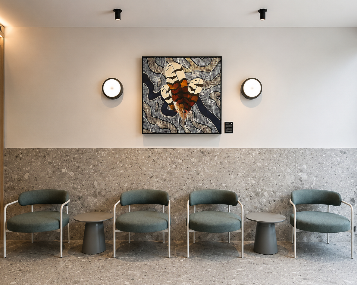 A row of four green seating chairs with white metal arms and legs in a modern waiting area, with two small round tables between the chairs. The background features a beige tiled lower wall, a white upper wall with a framed artwork of a butterfly, and two round wall lamps on either side of the artwork.