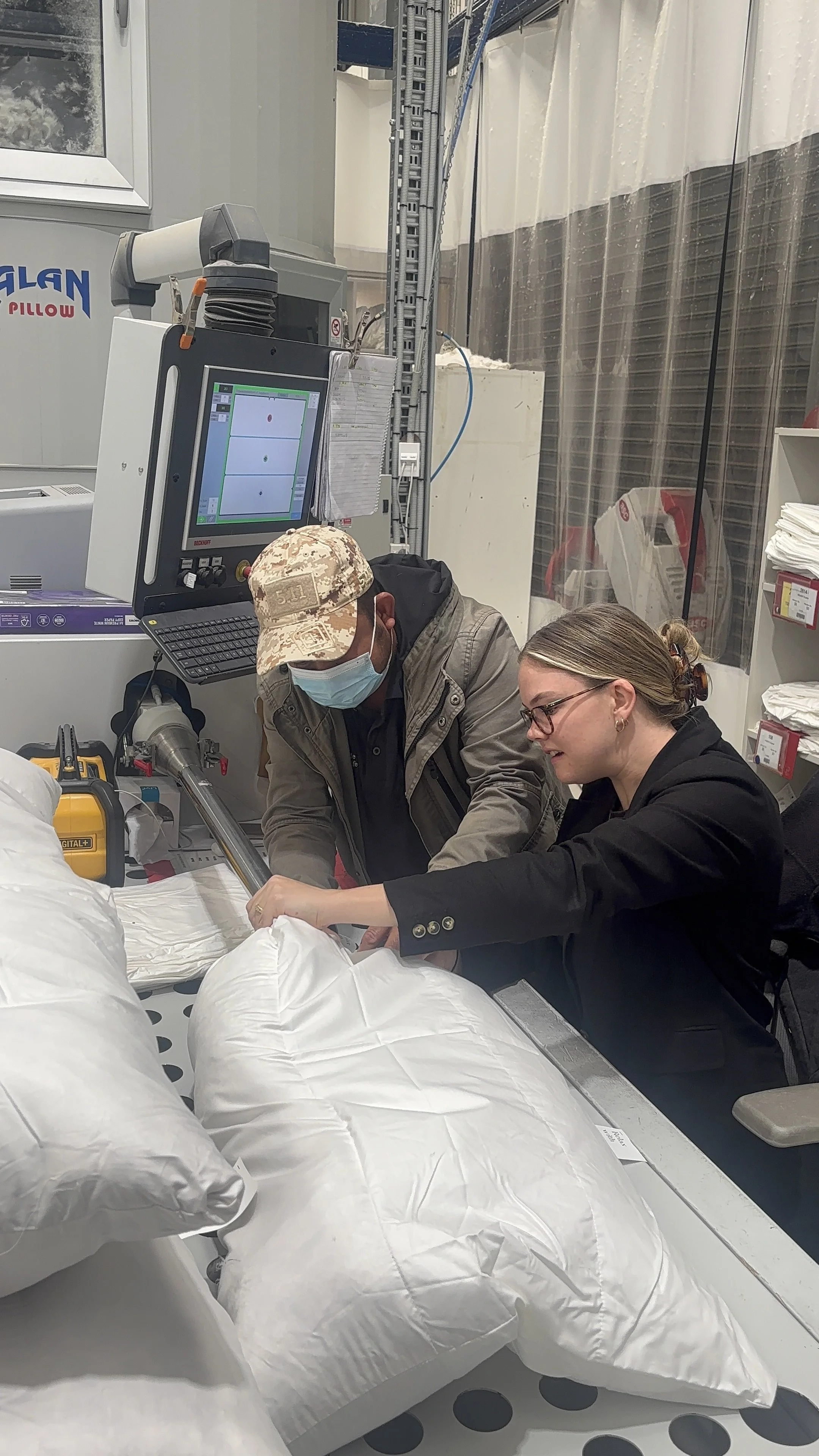 Two people working with large white bags in a medical or laboratory setting, with monitoring equipment visible in the background.