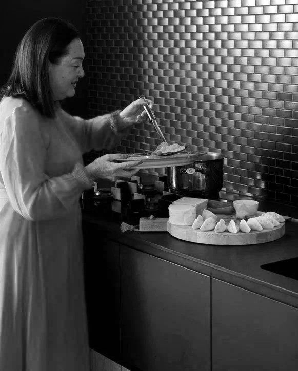 Woman serving cheese in a modern kitchen with a metallic tile backsplash.