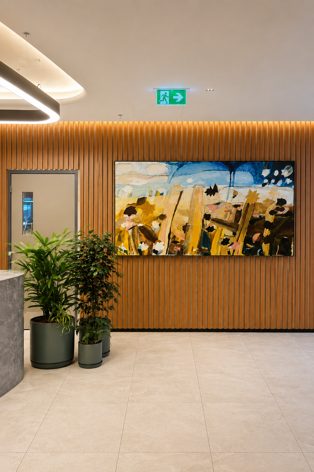 Interior of a modern building lobby with a wooden slat wall, a colorful abstract painting, potted green plants, and a ceiling exit sign.