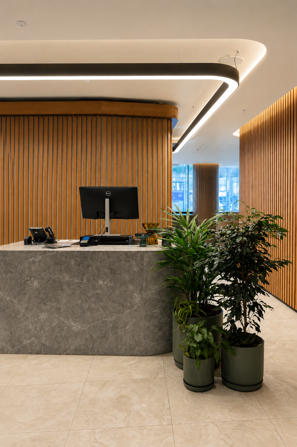 Reception desk in a modern office with a computer, phone, and decorative plants against wood-paneled walls and large windows.