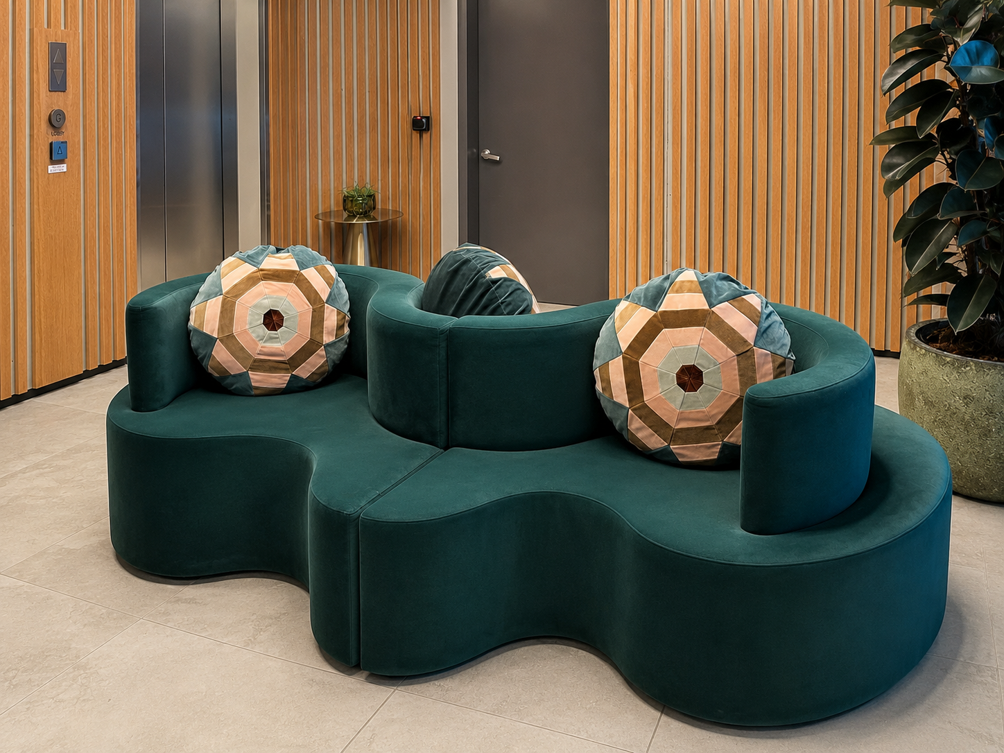 Modern lobby seating area with green curved sofa and patterned pillows, wood-paneled walls, elevator, and potted plant.
