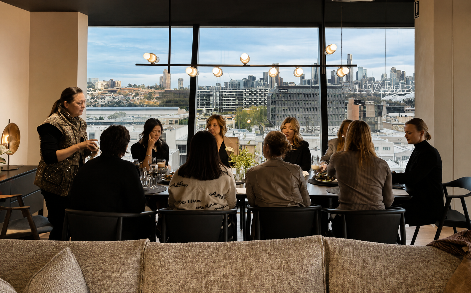Group of people sitting at a dining table during a meal in a high-rise restaurant with a city skyline view through large windows.