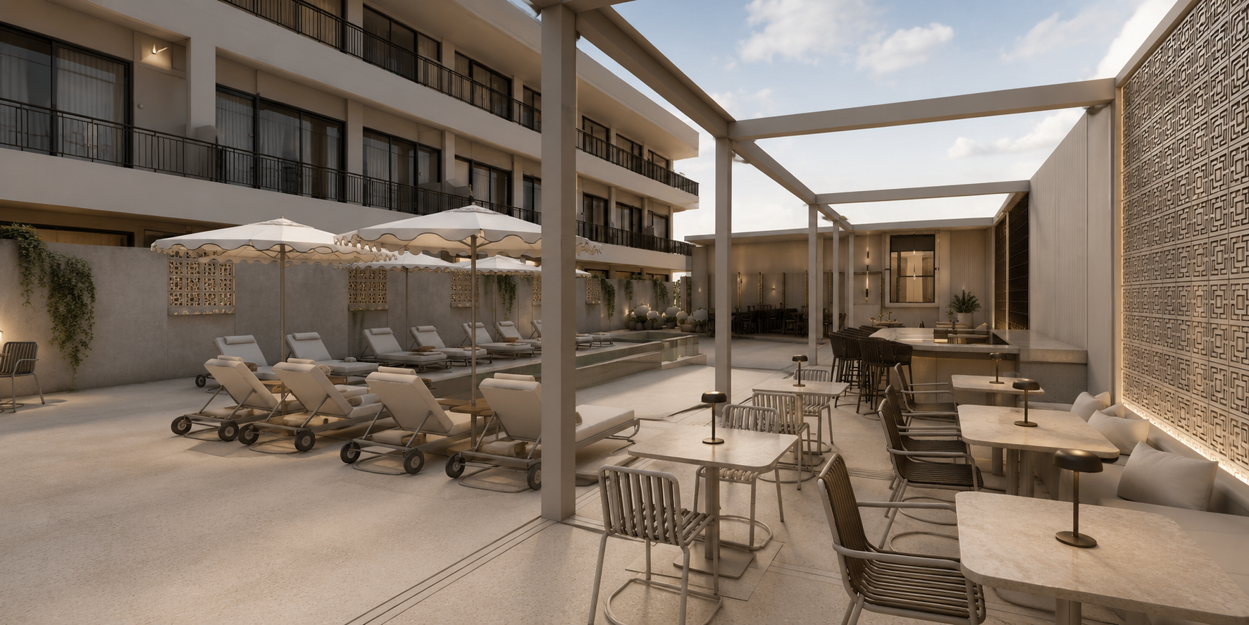 A modern outdoor hotel lounge area featuring lounge chairs with umbrellas, club chairs, tables, and a bar with seating, set against a backdrop of a building with balconies, decorative wall panels, and a partly cloudy sky.