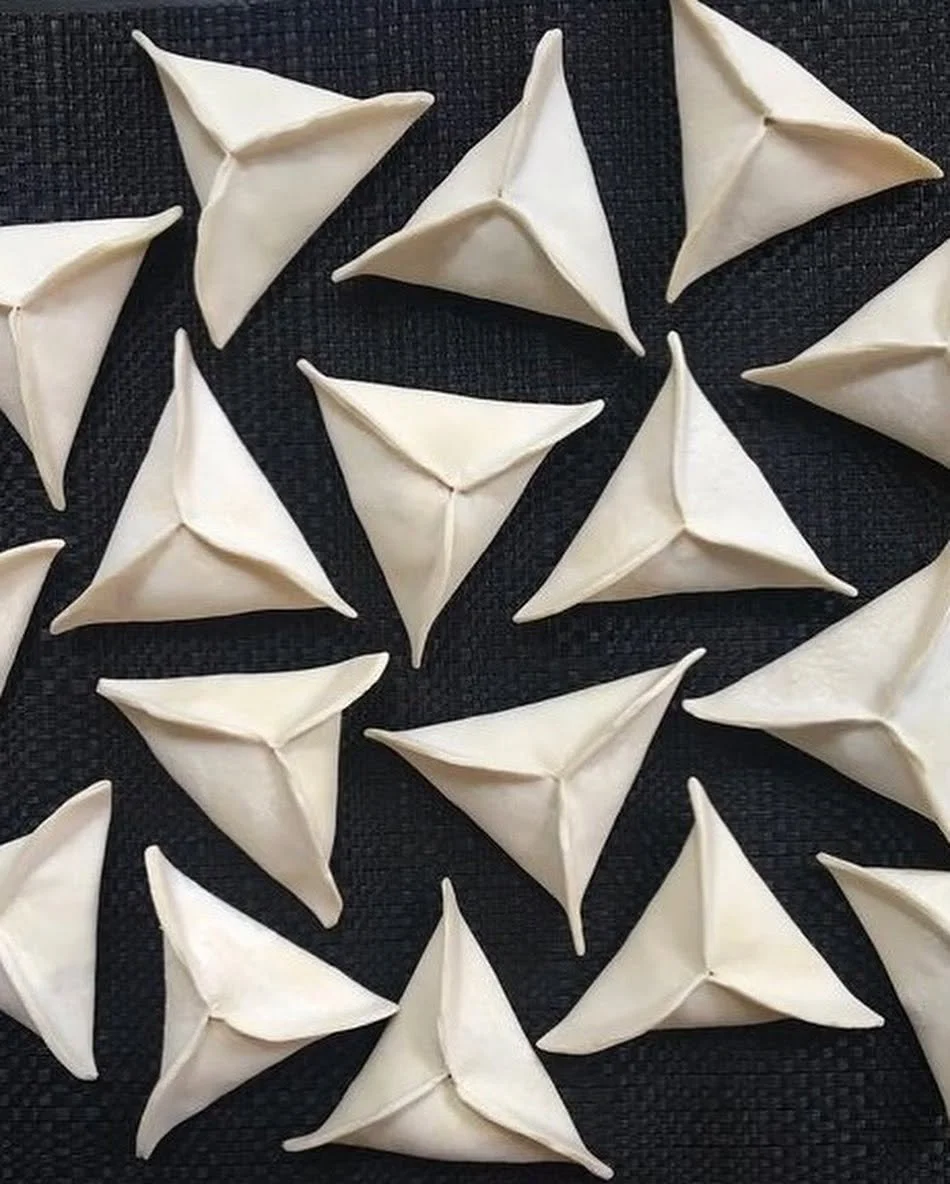 Several uncooked samosas arranged on a black textured surface.