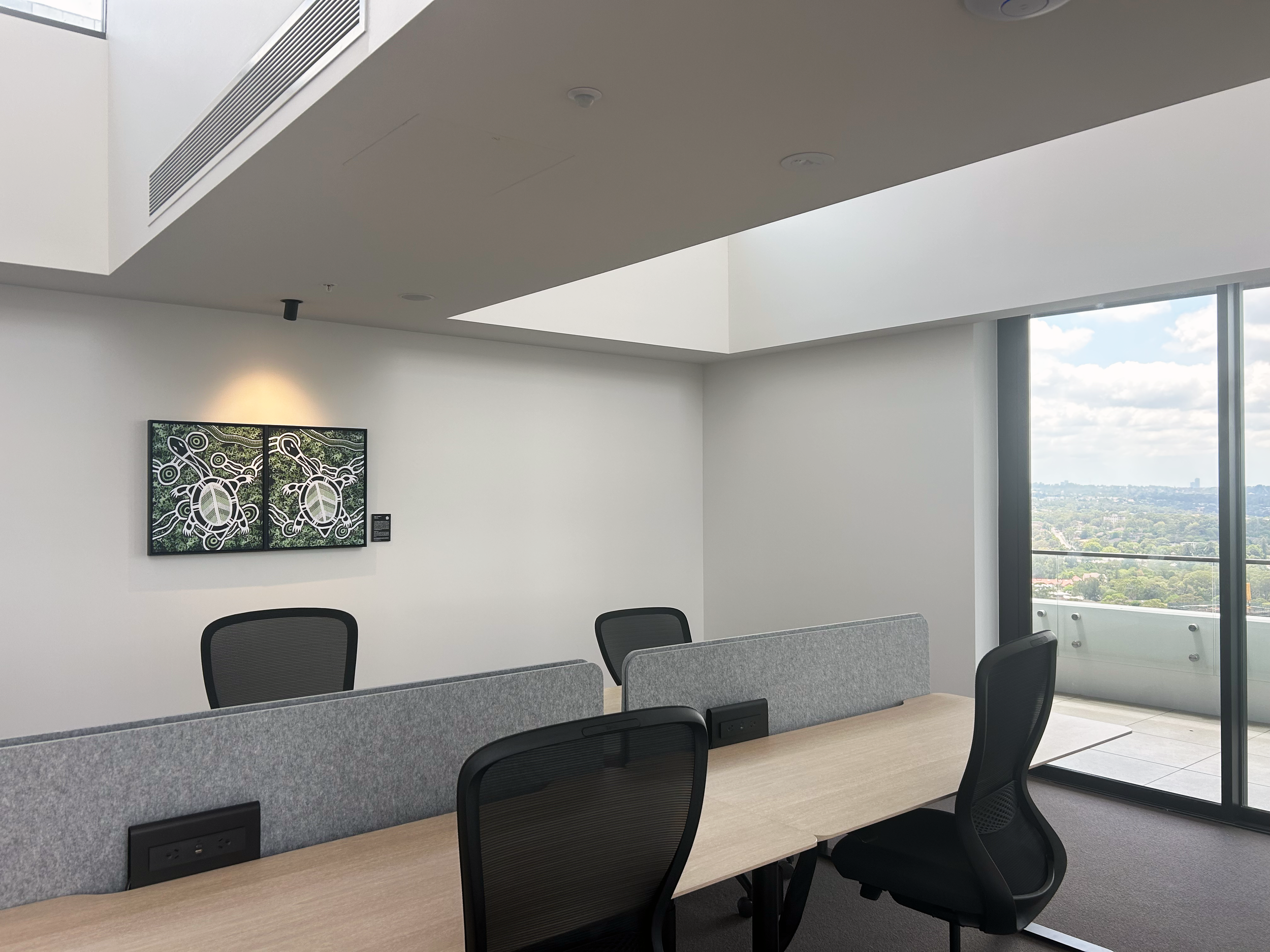 Modern conference room with long wooden table, ergonomic chairs, artwork on the wall, large window with a city view, and ceiling lights