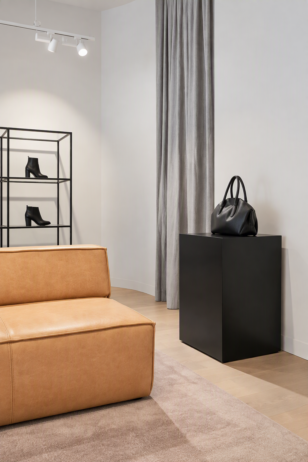 Interior of a modern living room with a tan leather sofa, a black display shelf with black ankle boots, gray curtains, and a black pedestal with a black handbag on top.