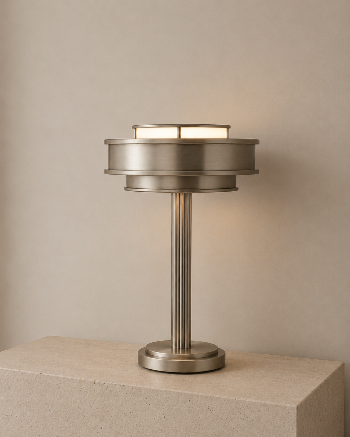 Modern metallic table lamp with a cylindrical base and a round shade, placed on a beige surface against a plain beige wall.