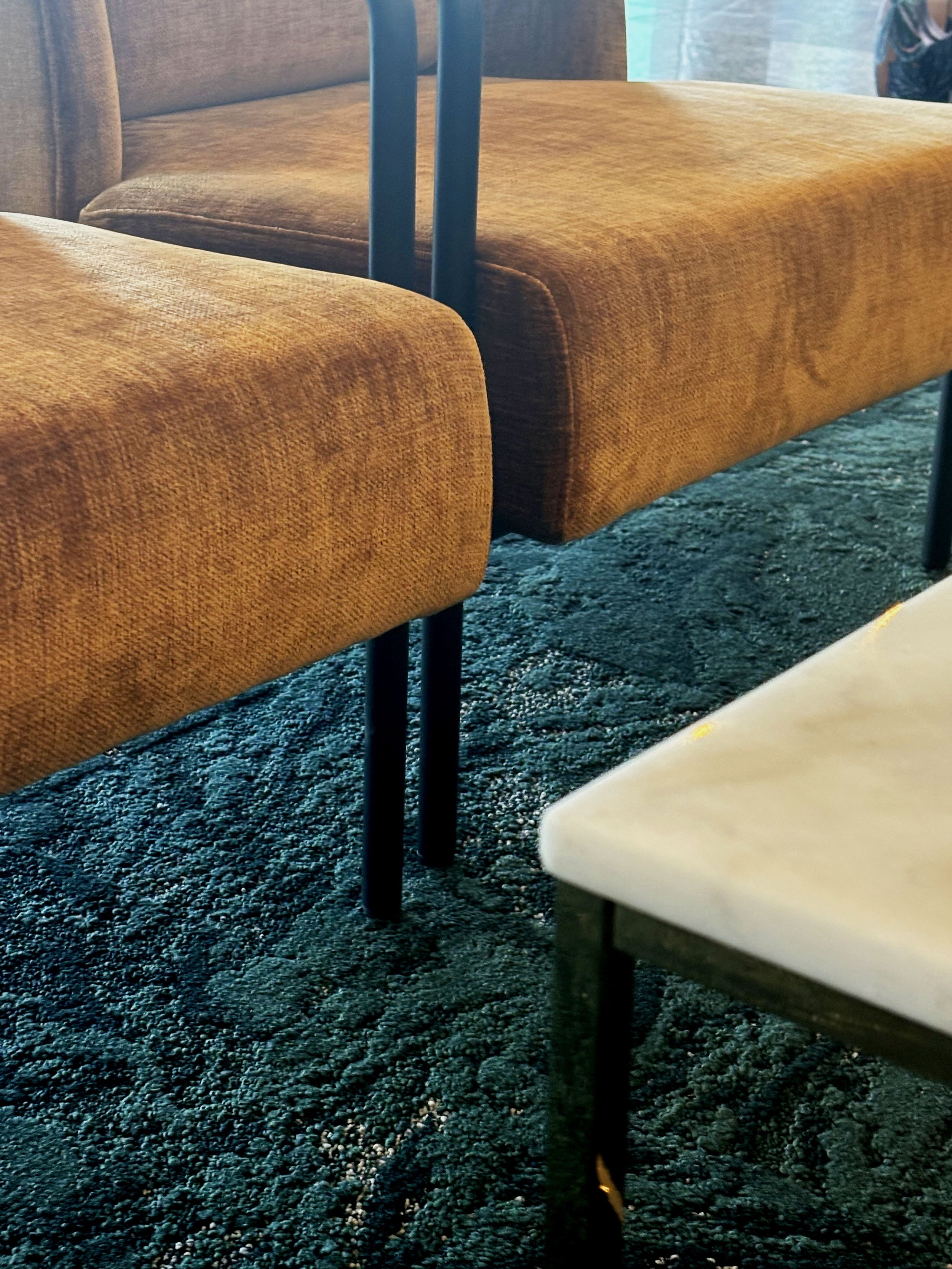 Close-up of brown upholstered chairs and part of a white table on a dark textured carpet.