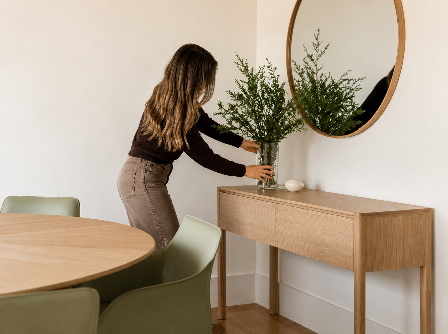 A woman arranging a vase with a plant on a sideboard in a modern dining room.