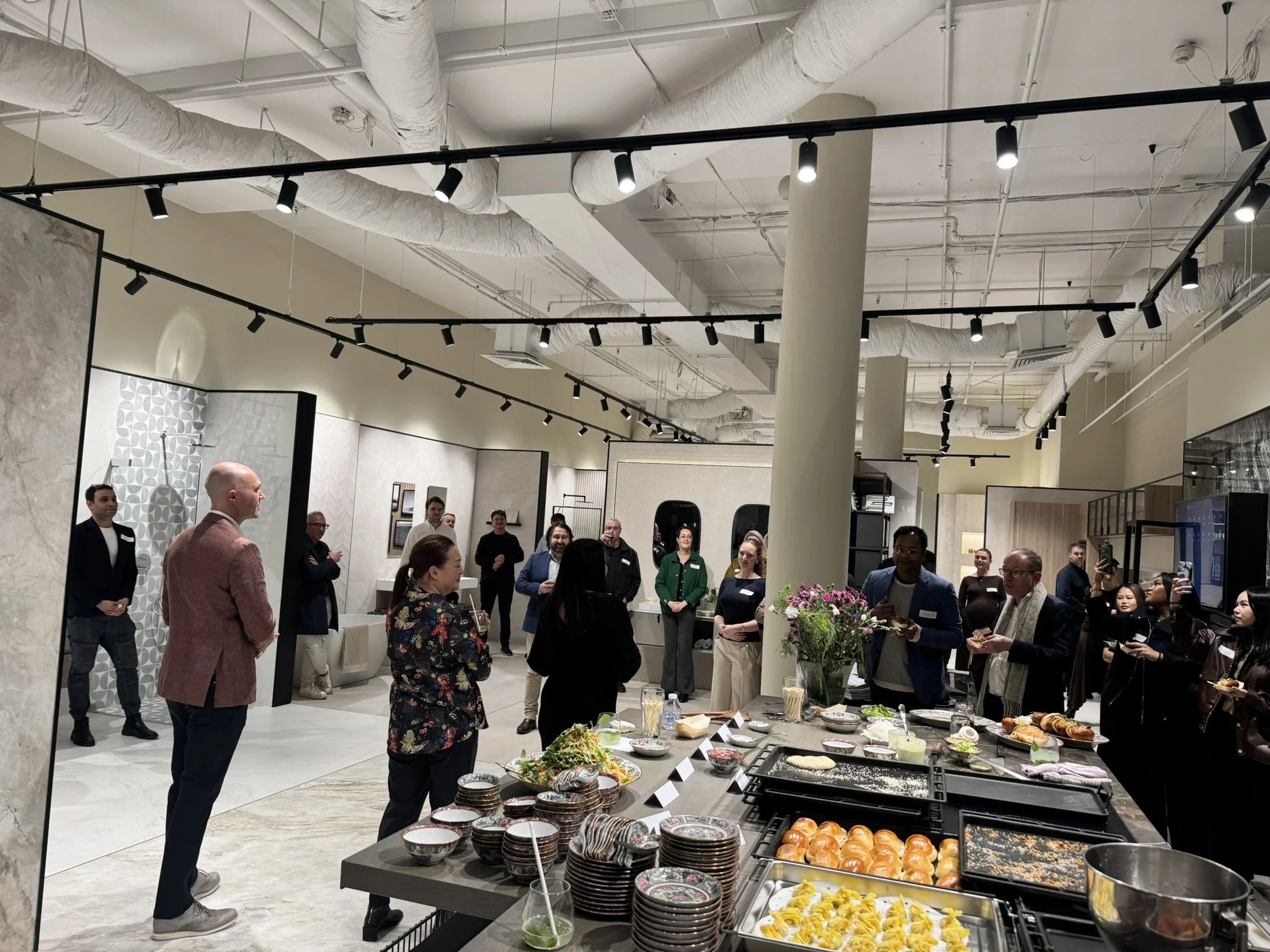 People gather at a buffet table with various dishes, in a modern, industrial-style event space with exposed ductwork and track lighting.
