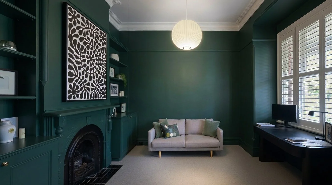 A living room with dark green walls, a white sofa with colorful pillows, a black TV stand with a small TV, and large windows with white shutters. A decorative fireplace is against the wall with built-in shelves and a lantern hanging from the ceiling.