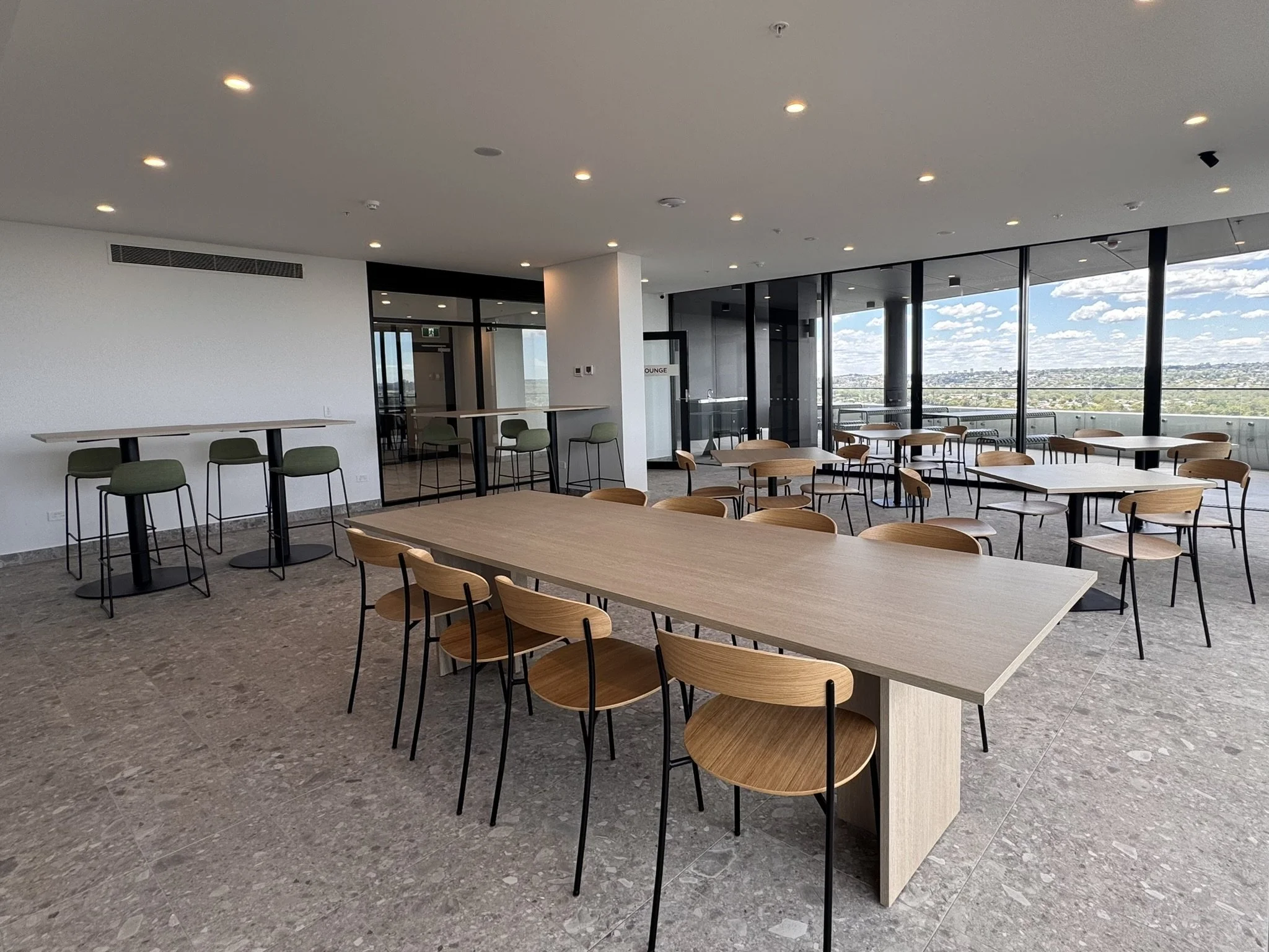 Empty lounge area with high tables and stools, and low tables with chairs, large windows showing city view, modern interior design